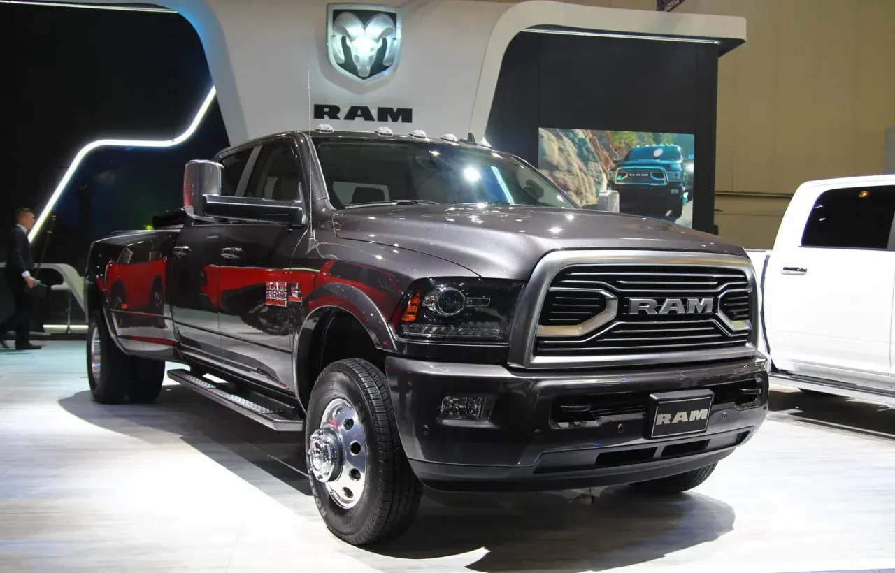 Ciemnoszary Dodge Ram 3500 z podwójnymi tylnymi kołami prezentuje się na wystawie, obok białego pickupa.