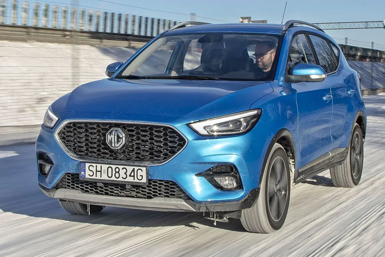 Niebieski MG ZS Classic jedzie po zaśnieżonej drodze. Kierowca w okularach prowadzi auto.