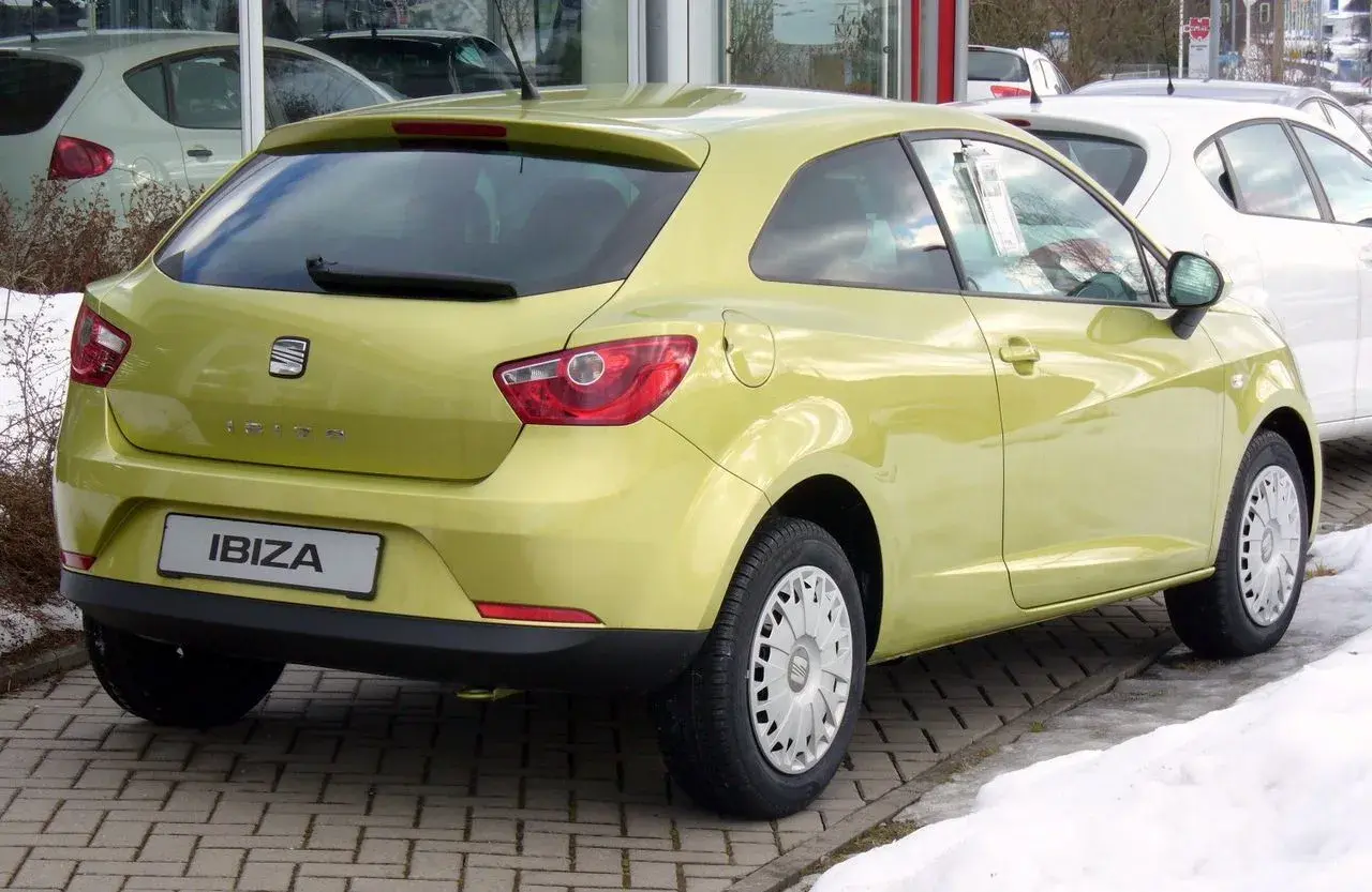 Jasnożółty Seat Ibiza 1.4 benzyna z tyłu, zaparkowany na kostce brukowej, obok śniegu.