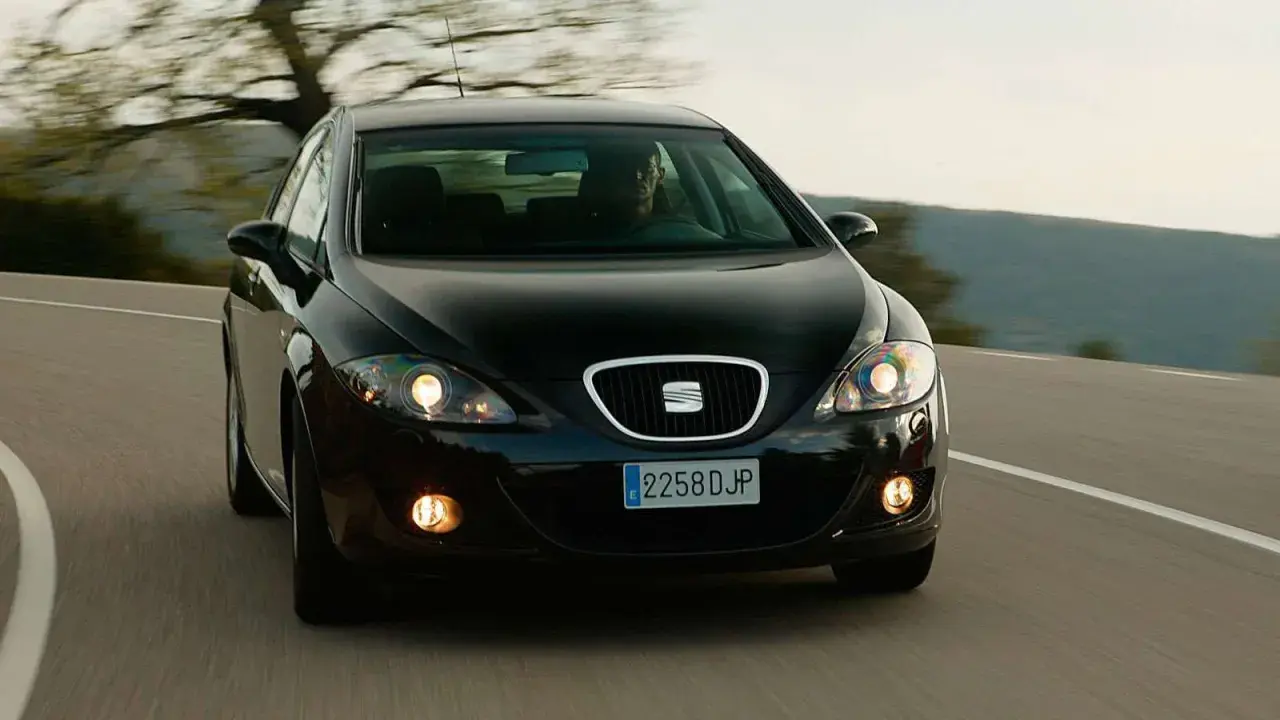 Czarny Seat Leon 2 jedzie po krętej drodze wśród drzew.