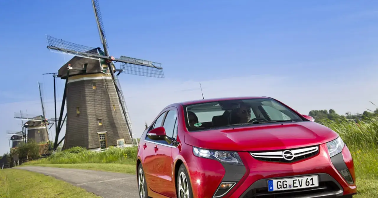Czerwony Opel Ampera na tle wiatraków w Holandii.