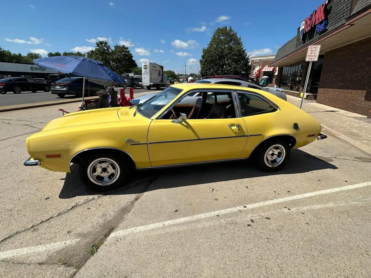 Żółty Ford Pinto z lat 70. stoi zaparkowany przy ulicy, obok sklepu.