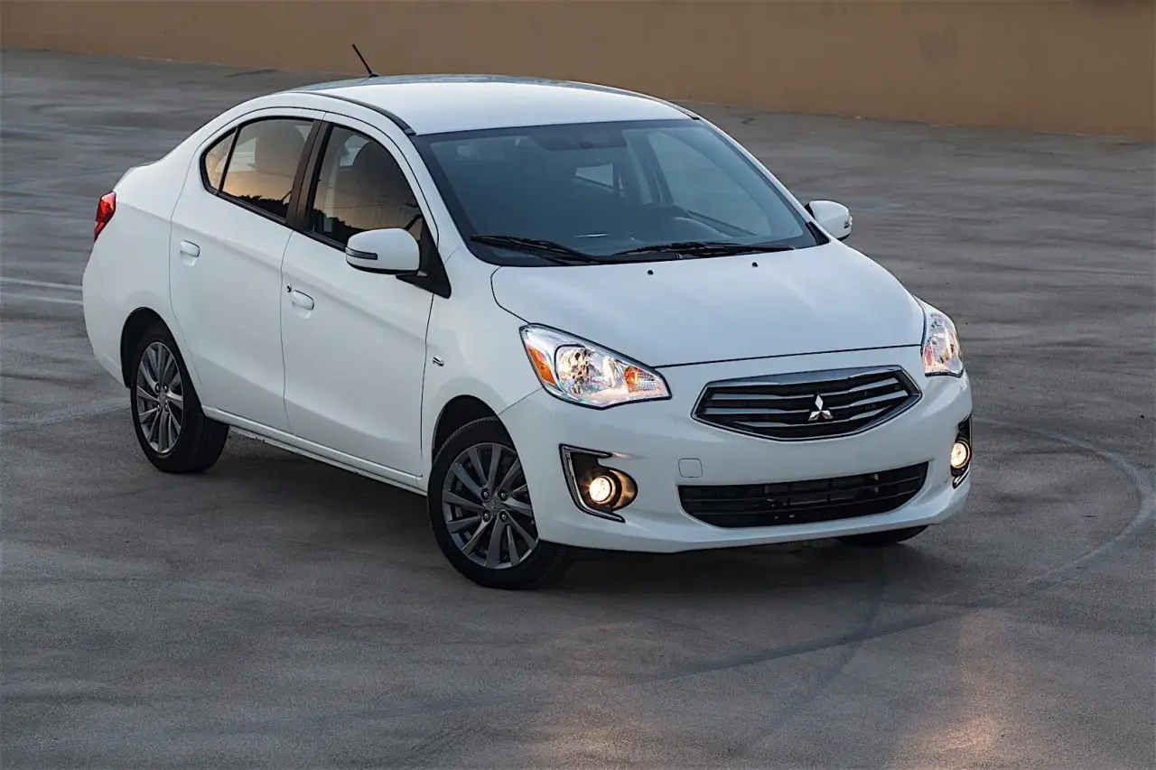 Biały sedan Mitsubishi Mirage zaparkowany na betonowej nawierzchni.