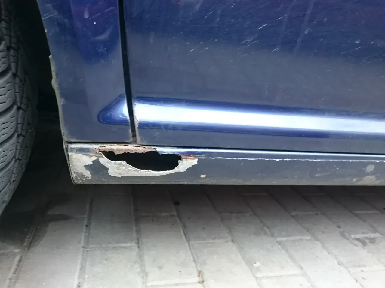 Widoczne są poważne dziury w progach niebieskiego samochodu, co pokazuje, jak załatać dziury w samochodzie.
