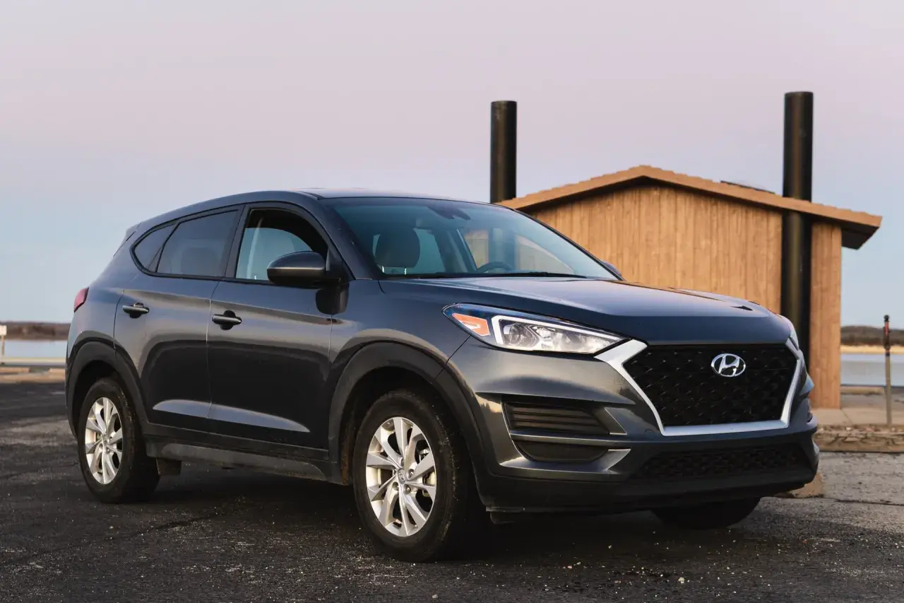 Ciemnoszary Hyundai Tucson zaparkowany przy drewnianej budowli. Zastanawiasz się, ile pali ten model?