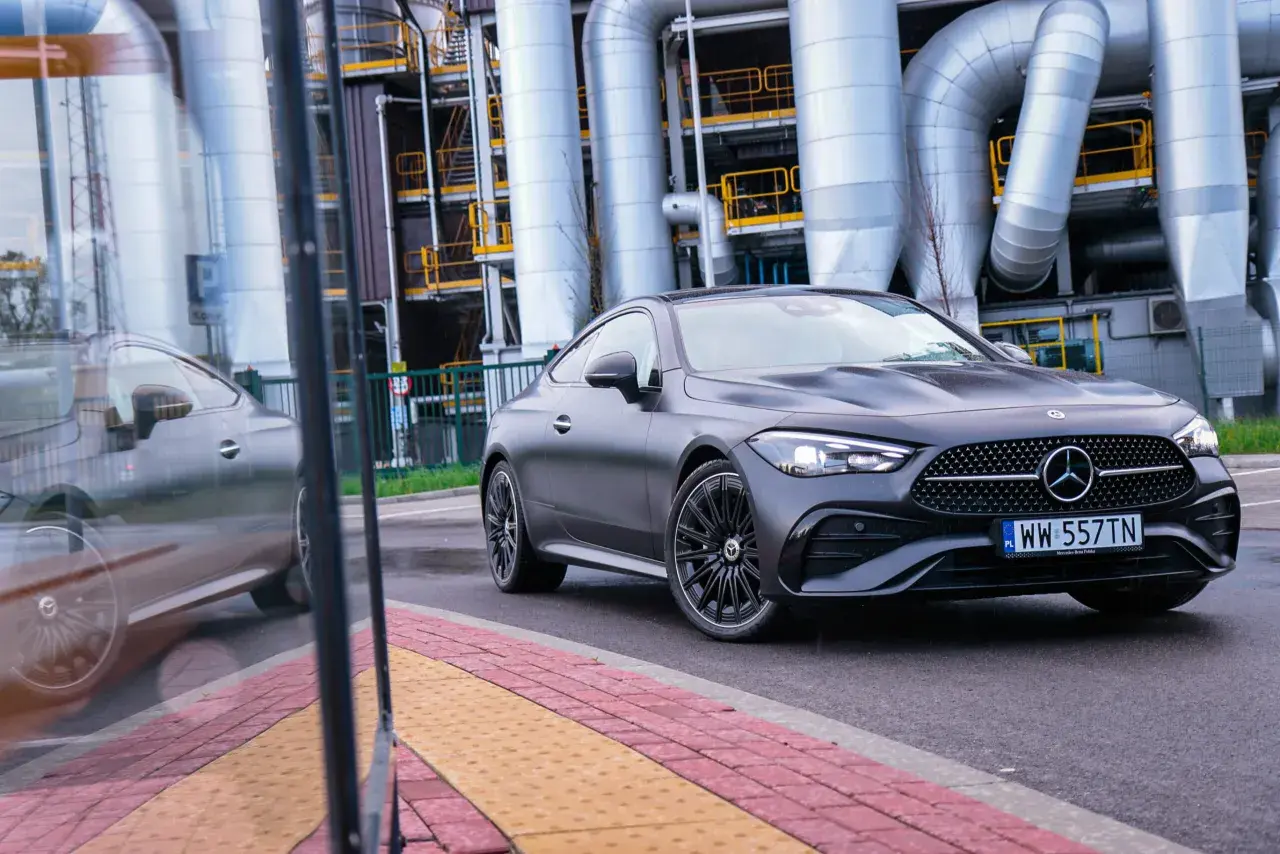 Ciemnoszary Mercedes-Benz CLE Coupé na tle przemysłowych rur i budynków.