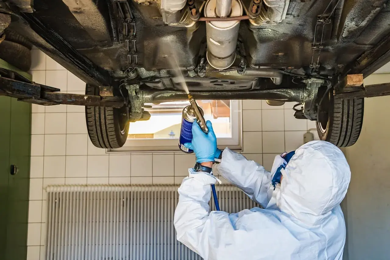 Mechanik w kombinezonie ochronnym zabezpiecza podwozie auta. Zastanawiasz się, ile kosztuje przegląd samochodu z gazem?