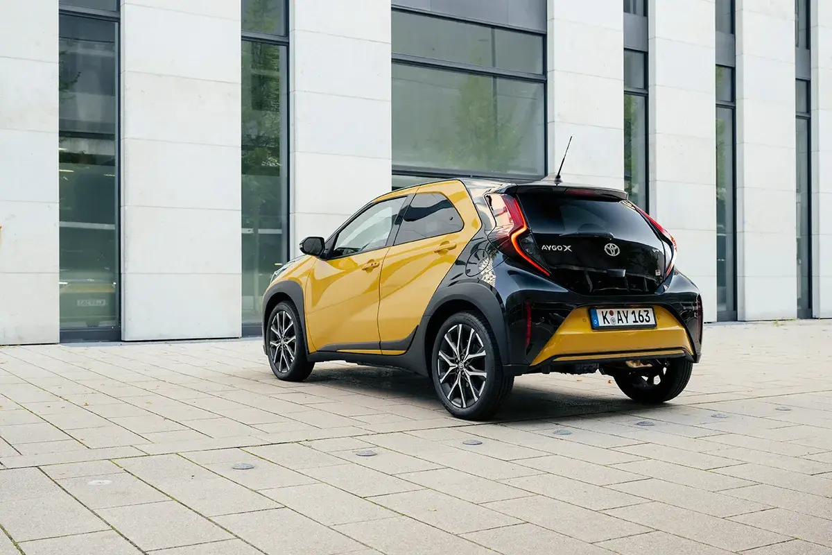 Żółto-czarny crossover Toyota Aygo X stoi na placu przed nowoczesnym budynkiem.