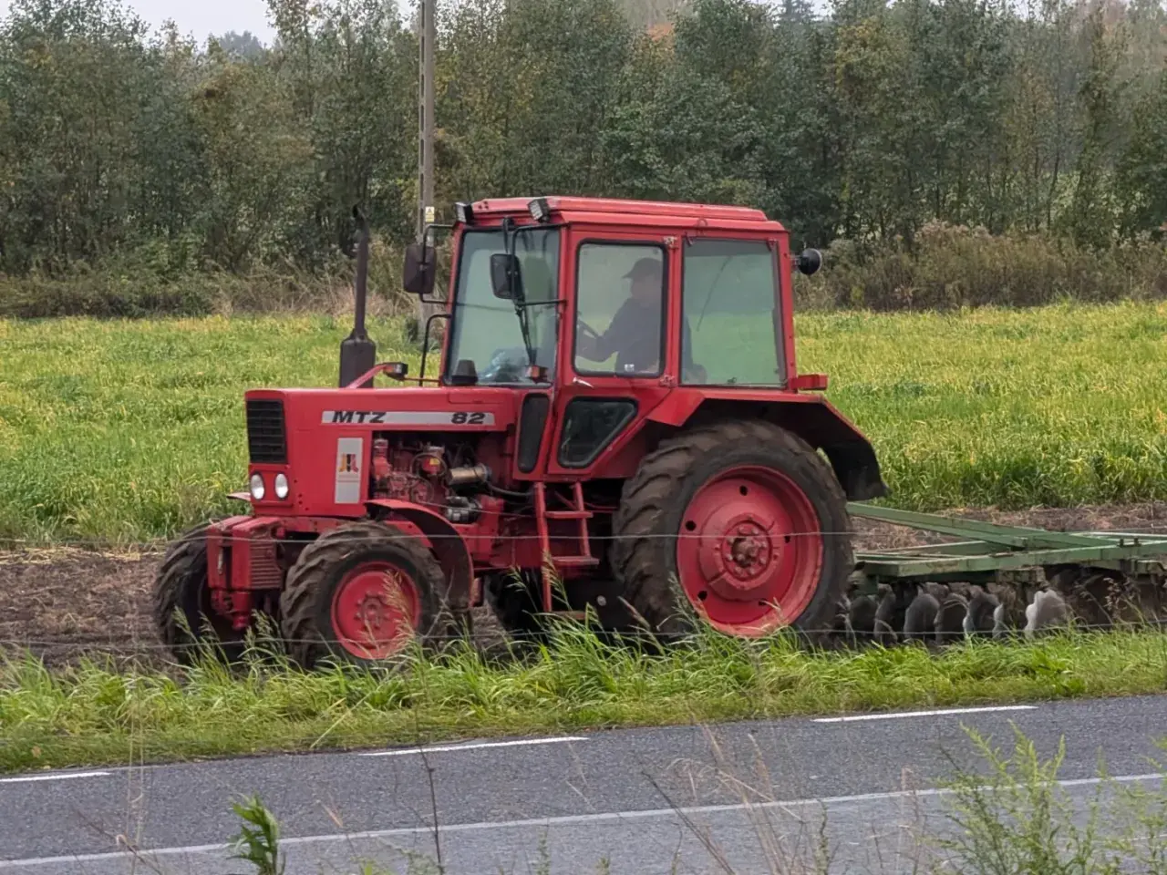 Czerwony ciągnik MTZ Belarus 82 z kabiną pracuje na polu, za nim widać pług.