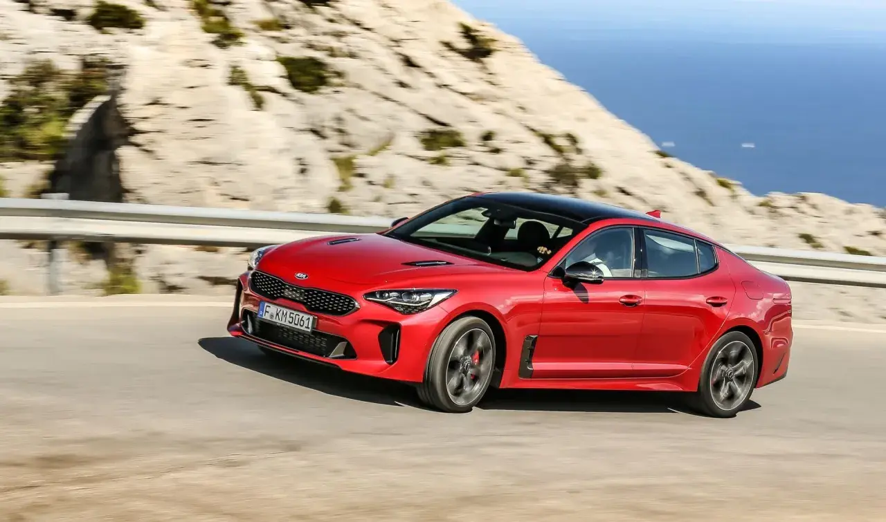 Czerwony Kia Stinger GT pędzi po krętej drodze z widokiem na morze.