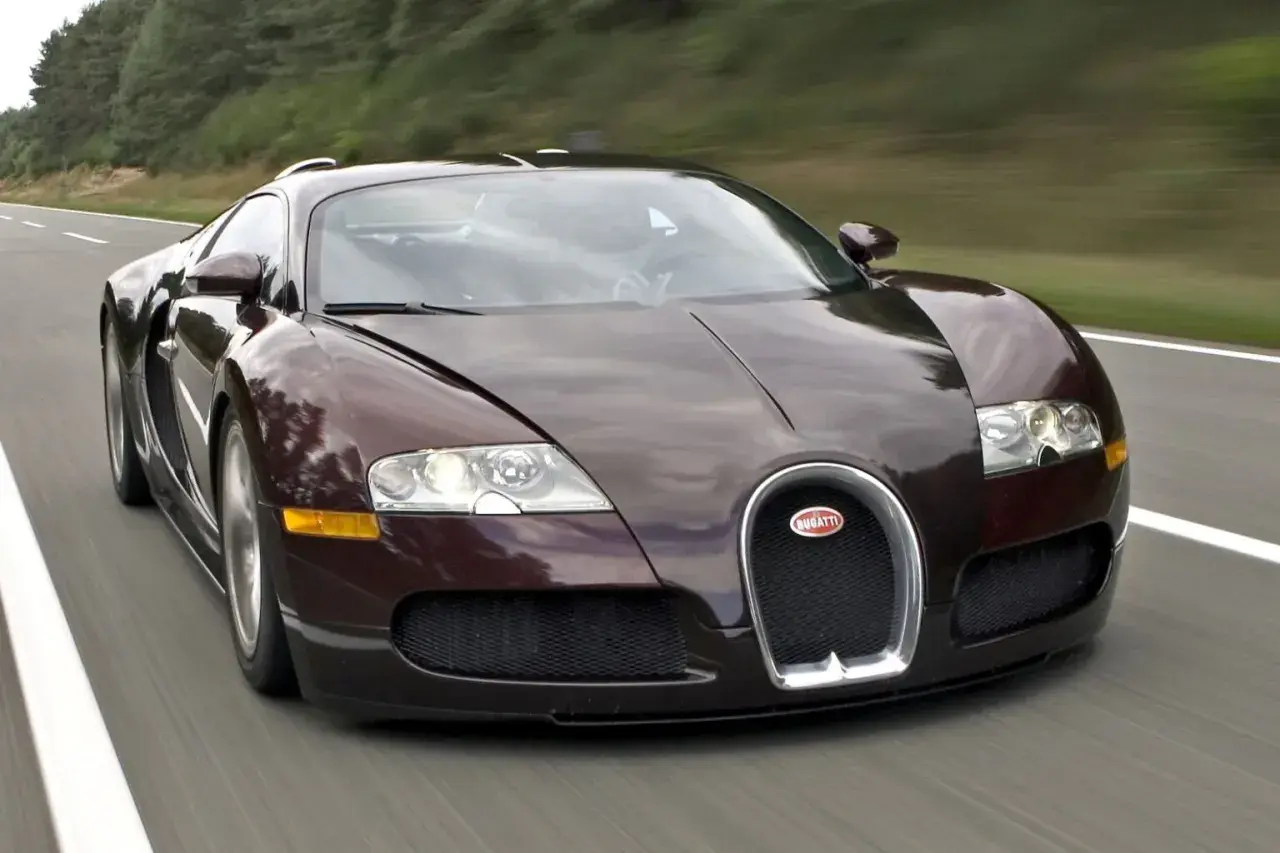 Ciemnobrązowy Bugatti Veyron pędzi po drodze. Ten hipersamochód ma 16 cylindrów, co przekłada się na jego niesamowitą moc.