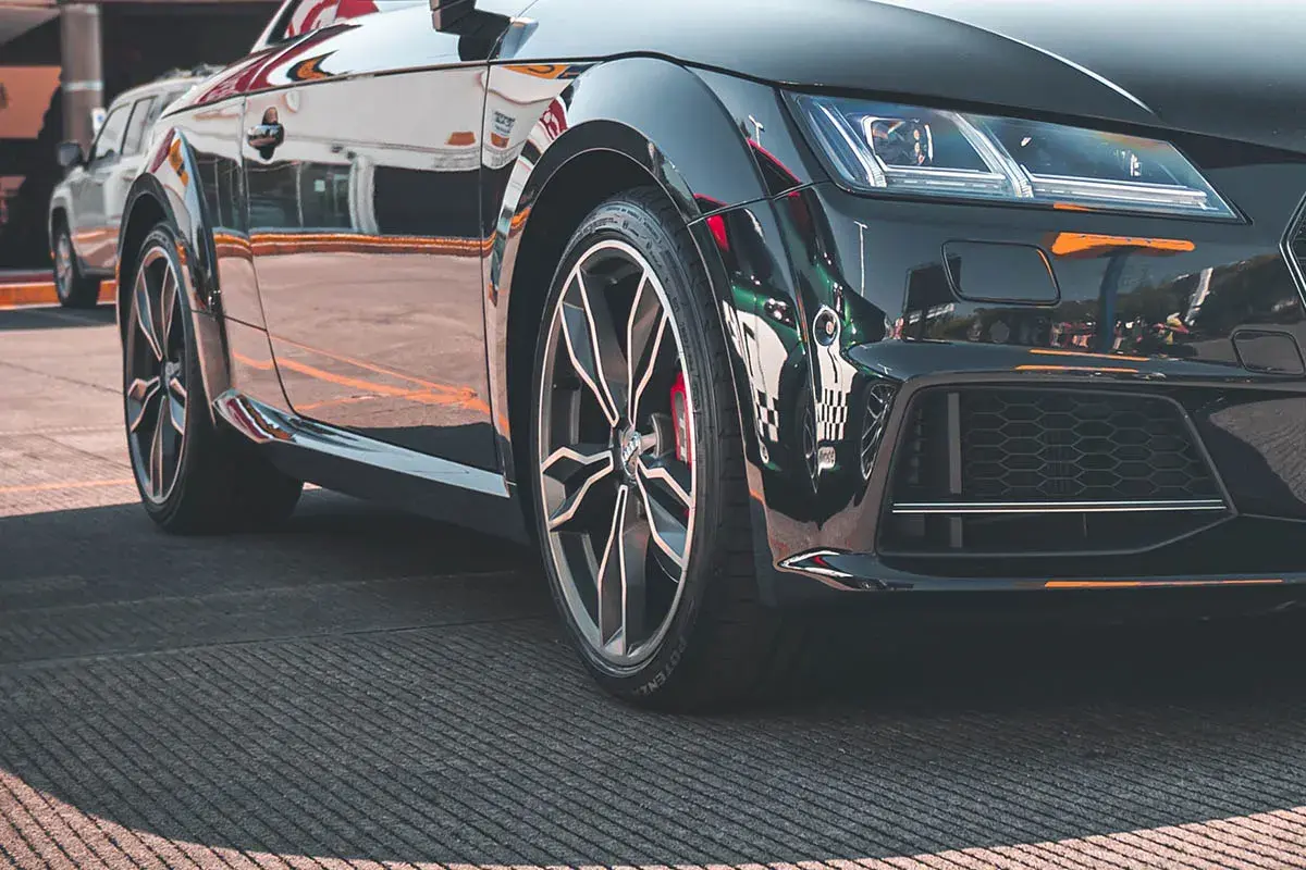 Zbliżenie na czarne, sportowe auto z widoczną felgą i oponą.