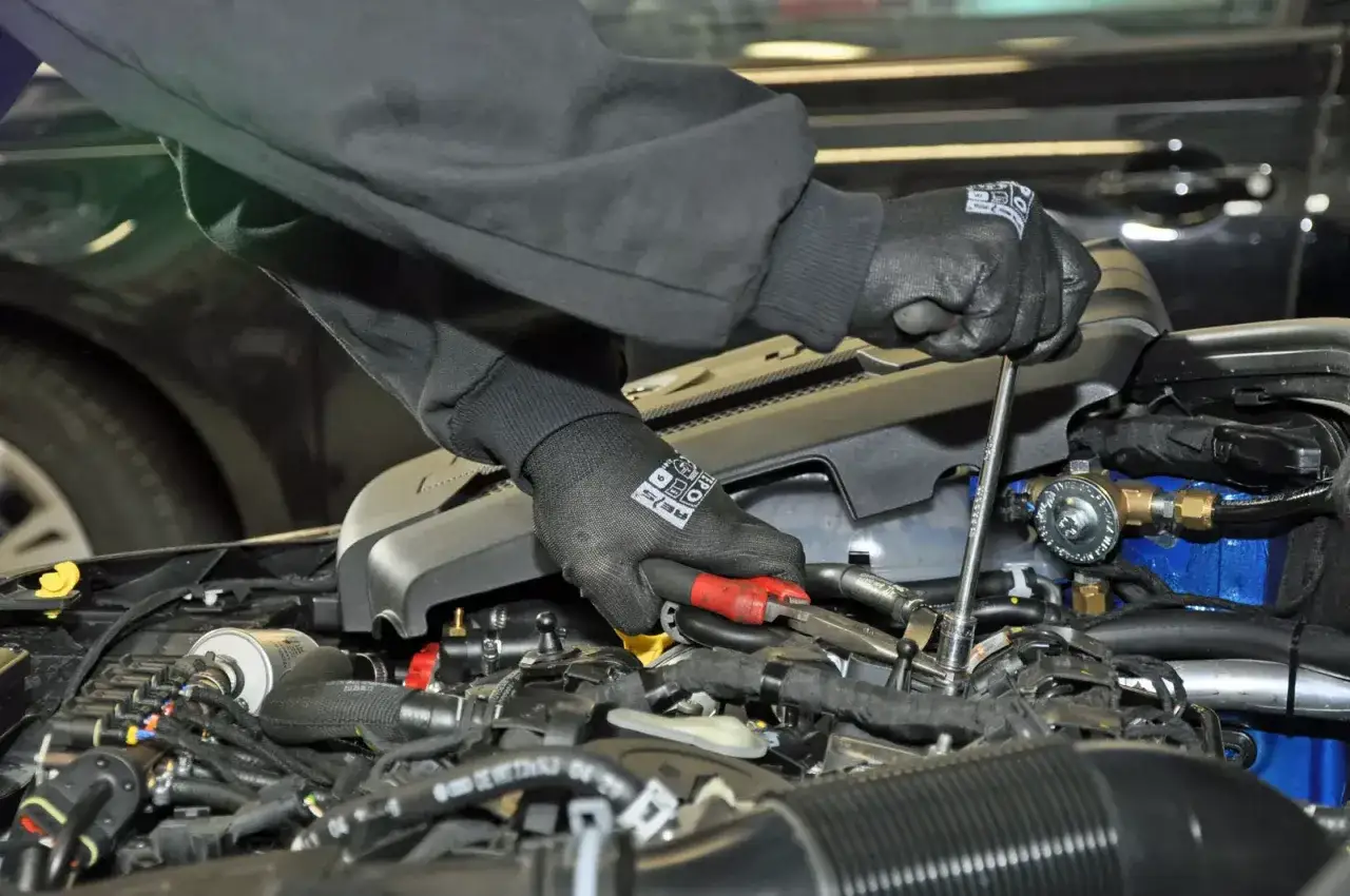 Mechanik w rękawiczkach montuje elementy instalacji gazowej w silniku. Zastanawiasz się, ile kosztuje założenie gazu?