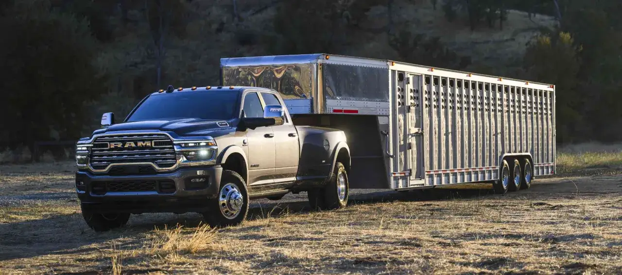 Ciemnoszary Dodge Ram 3500 z podwójnymi tylnymi kołami holuje dużą przyczepę do przewozu zwierząt.