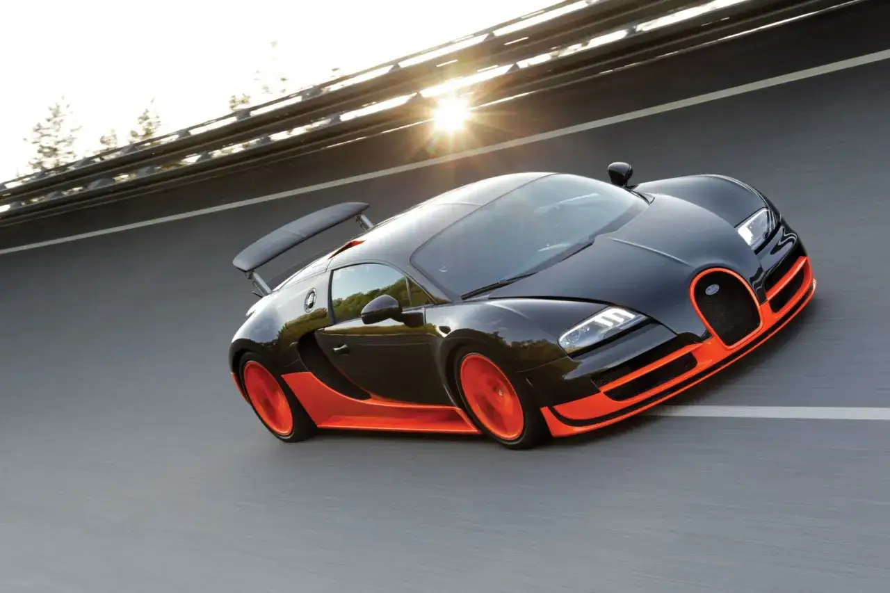 Czarny Bugatti Veyron z pomarańczowymi akcentami pędzi po drodze. Zastanawiasz się, ile koni ma Bugatti Veyron?