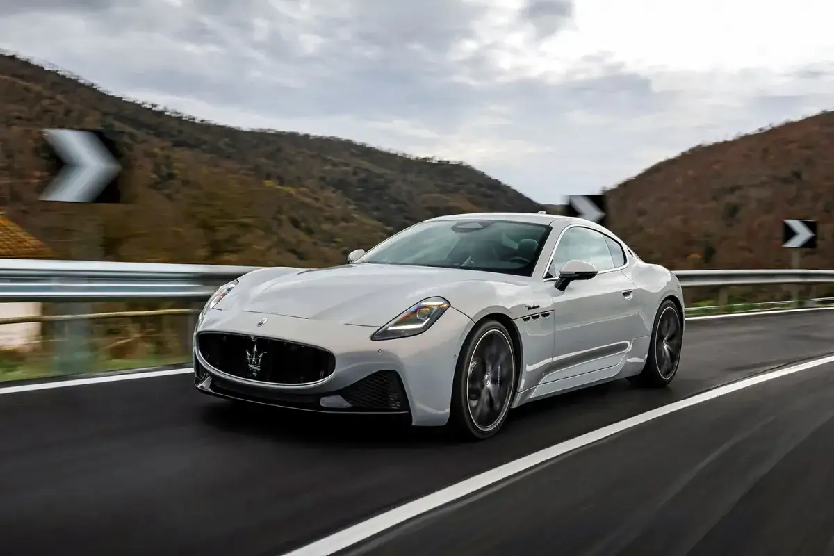 Srebrne Maserati pędzi po krętej drodze wśród wzgórz.