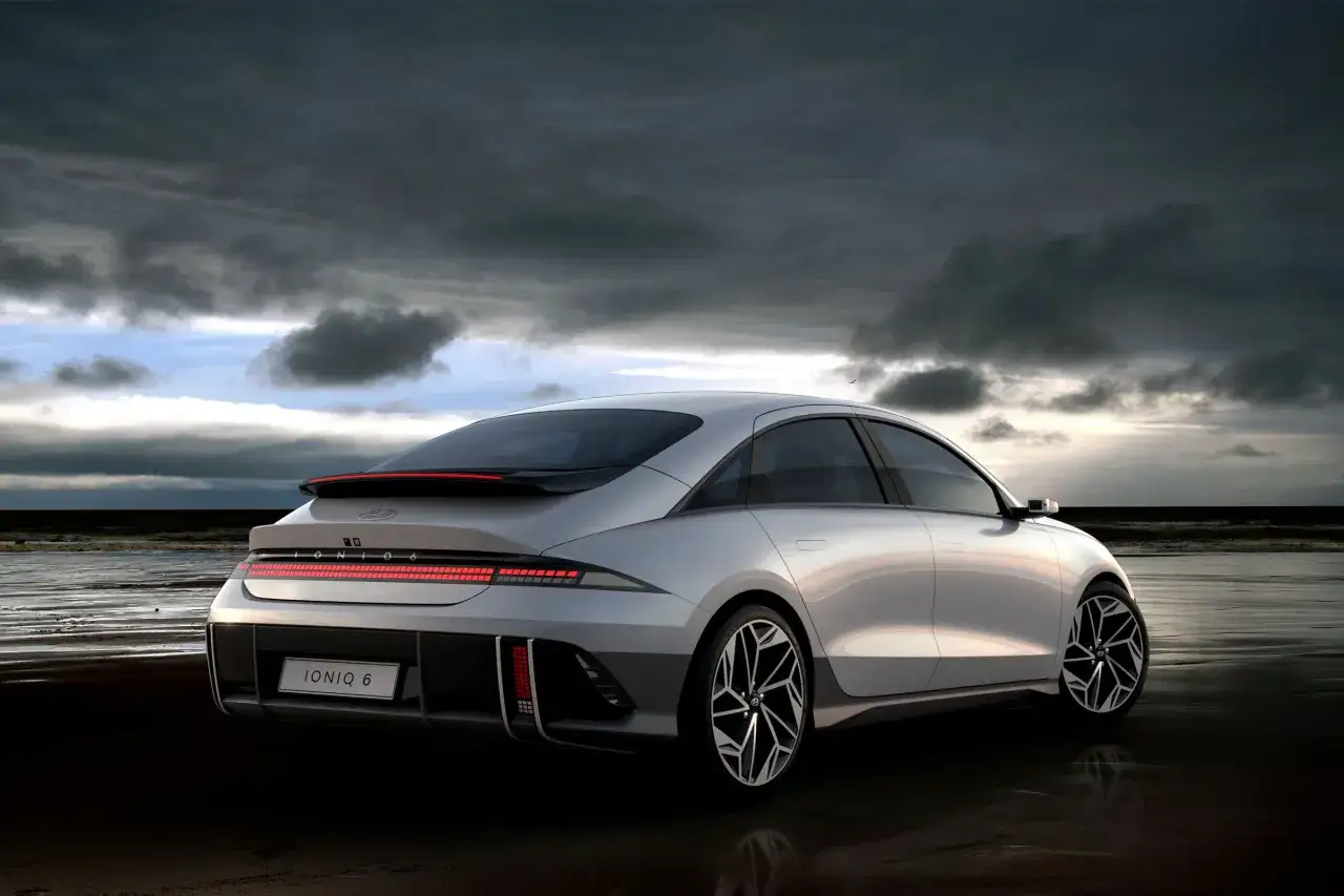 Srebrny Hyundai Ioniq 6 na mokrym piasku plaży, pod burzowym, dramatycznym niebem.