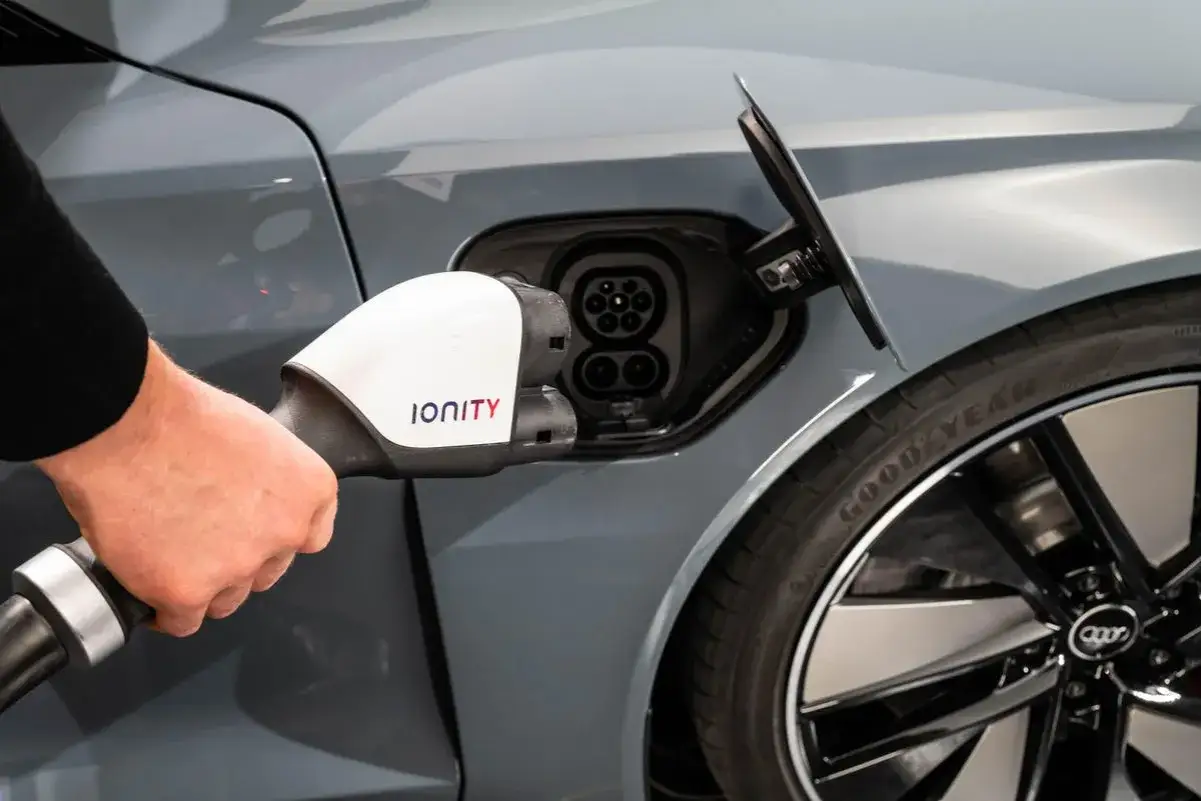 Ładowanie Audi e-tron GT. Dłoń trzyma wtyczkę Ionity, gotową do podłączenia do portu ładowania samochodu elektrycznego.