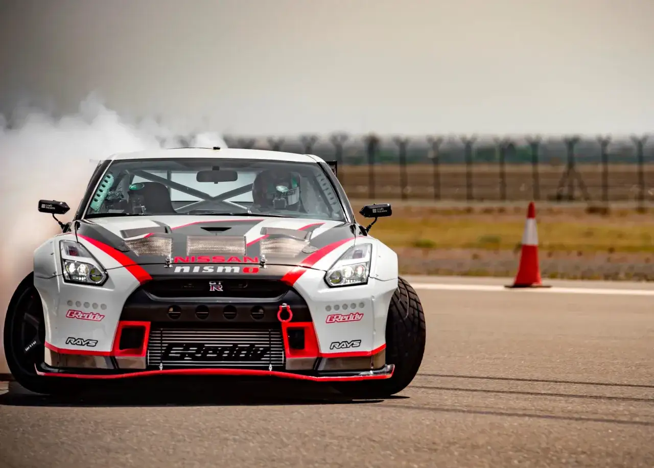 Biały Nissan GT-R Nismo z czerwonymi i czarnymi akcentami driftuje, generując kłęby dymu.