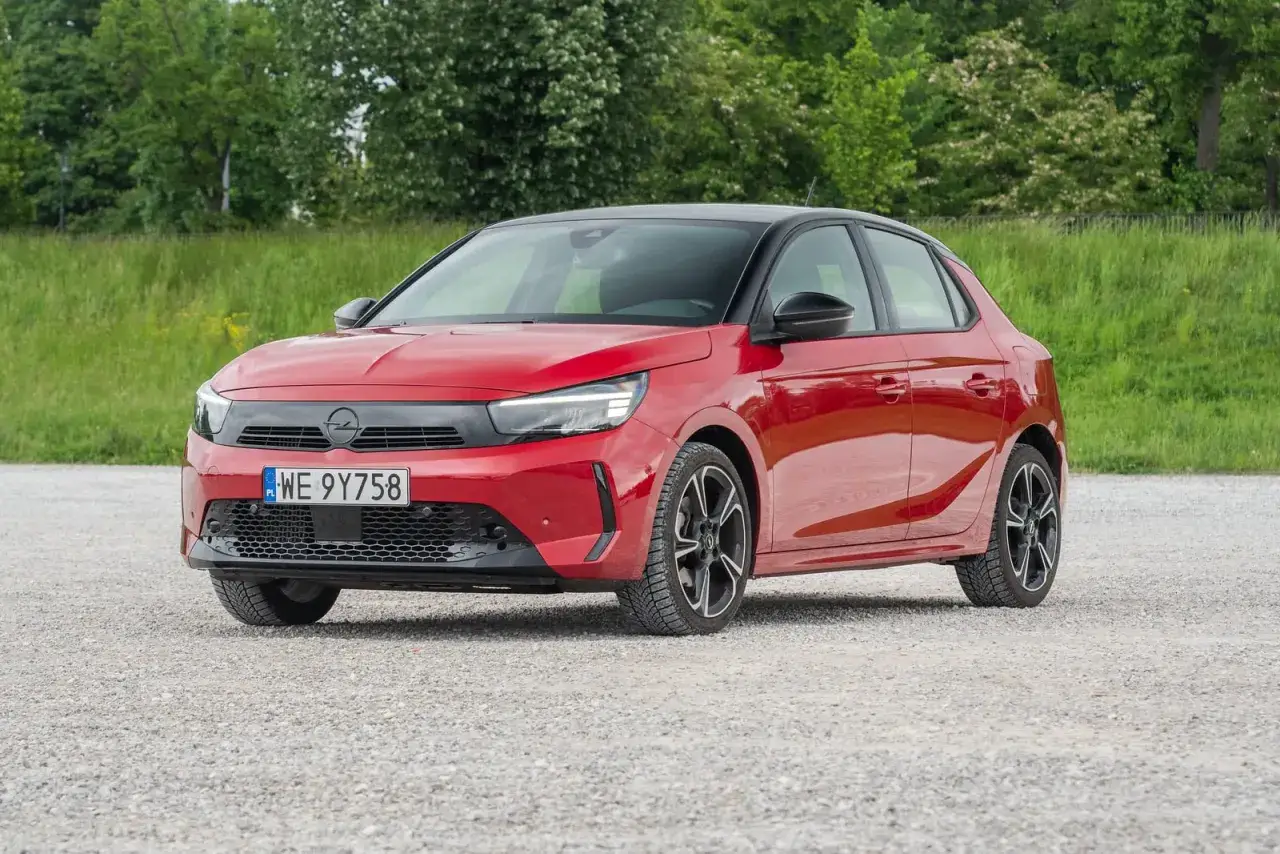 Czerwona Opel Corsa na tle zieleni. Zastanawiasz się, ile pali Opel Corsa? Ten model oferuje oszczędną jazdę.