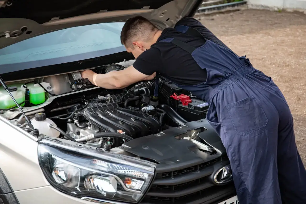 Mechanik w granatowym kombinezonie pracuje przy silniku diesla. W tle widać płyny do chłodnicy.