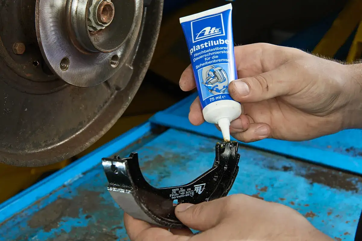 Mechanik nakłada smar ceramiczny do hamulców na szczękę hamulcową, przygotowując ją do montażu.