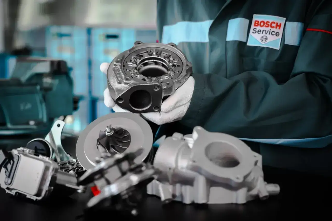Mechanik w kombinezonie Bosch Service prezentuje części turbosprężarki. Dowiedz się, jak sprawdzić turbinę i jej elementy.